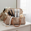 Beige handbag with hairbrush, hair products, and a flower on a light wooden surface.