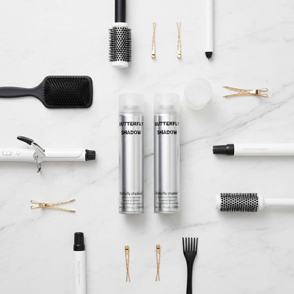 Butterfly Shadow hair spray makeup products with various hair styling tools on a marble surface