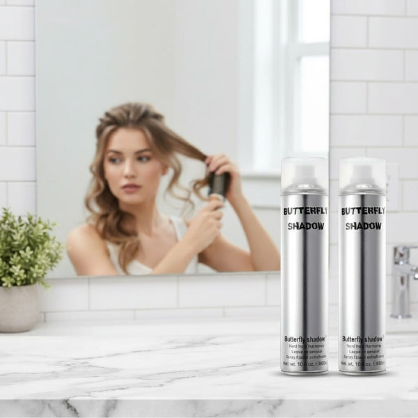 Woman styling her hair in front of a mirror with two bottles of 'Butterfly Shadow' products on a marble surface.